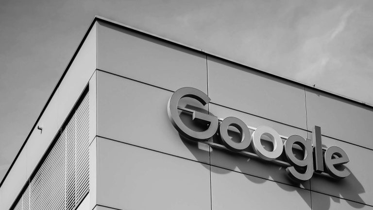 Black and white, low-angle shot of the Google logo on the side of a modern office building.