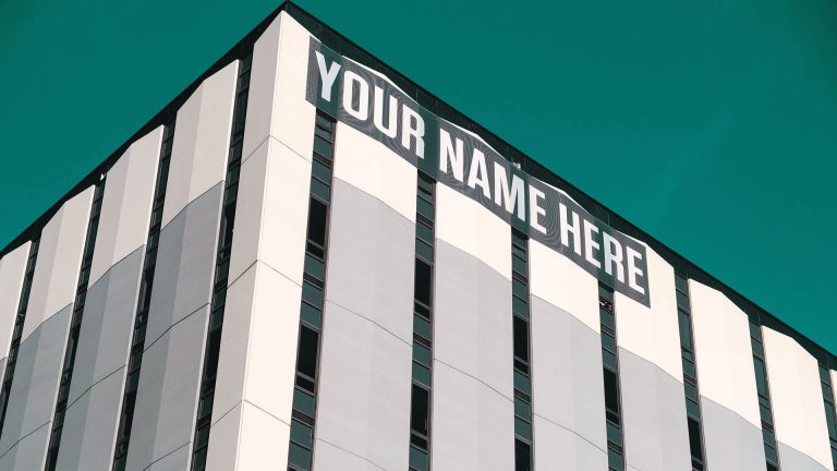 A large banner that reads "YOUR NAME HERE" on the side of a modern office building.