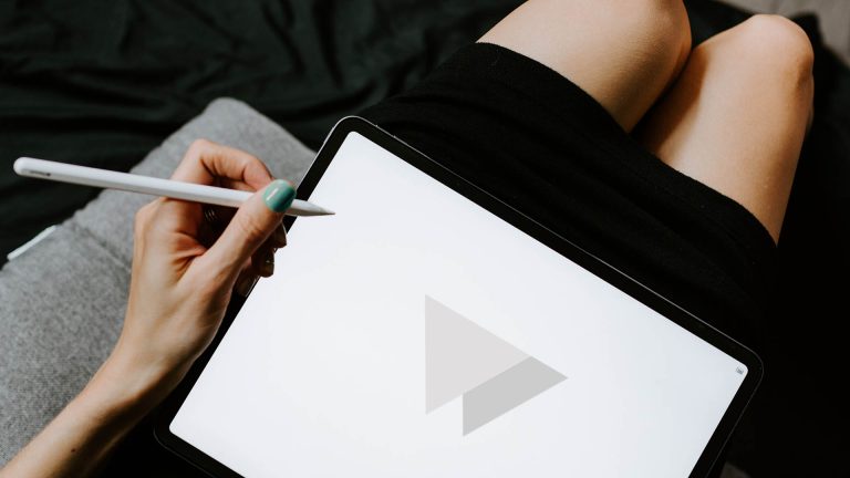 A person holding a stylus to a tablet screen that displays a minimalist grey logo.