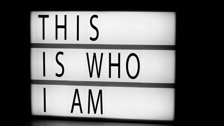 A glowing lightbox sign with the text "THIS IS WHO I AM" in a dark room.