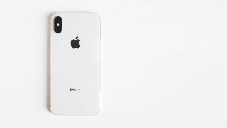 The back of a white and silver iPhone X lying on a plain white background.