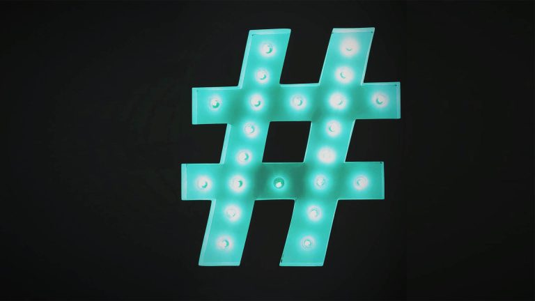 A light-up marquee sign of a hashtag symbol glowing teal against a black background.