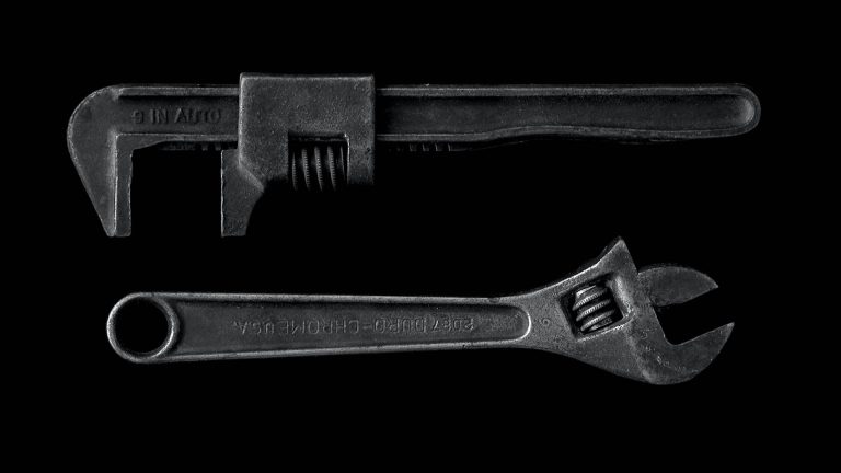 Two metal wrenches, a large auto wrench and a smaller adjustable wrench, on a black background.