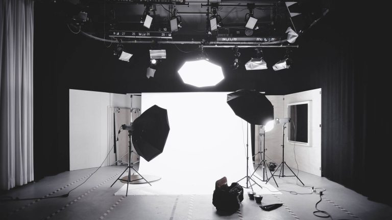 The interior of a professional photography studio with lighting equipment, softboxes, and a brightly lit white backdrop.