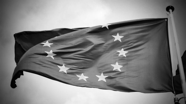 Black and white photo of the European Union flag waving against a cloudy sky.