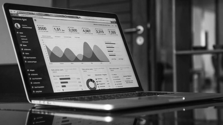 Black and white photo of a laptop screen displaying a data analytics dashboard with charts and graphs.