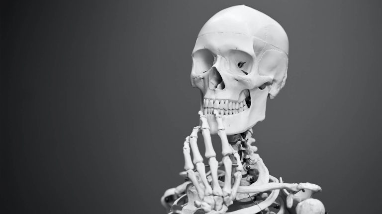 Black and white photo of an anatomical skeleton model in a classic thinking pose with its hand on its chin.