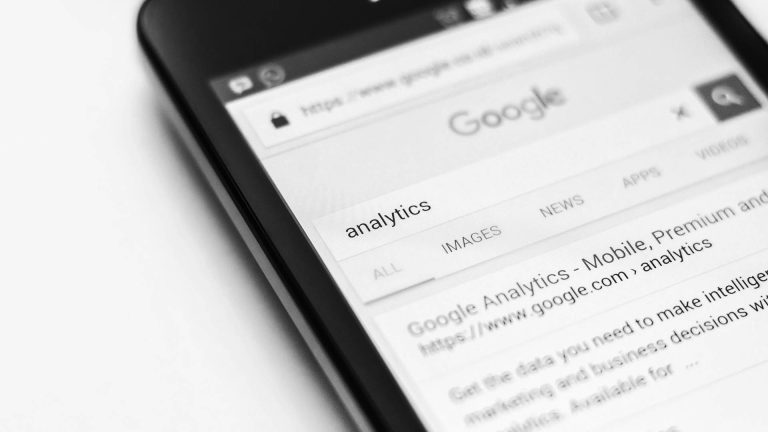 Black and white close-up of a smartphone screen showing a Google search for the word "analytics".