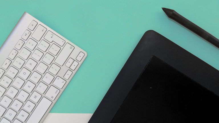 Top-down view of a graphics tablet, stylus, and keyboard on a teal and white background.