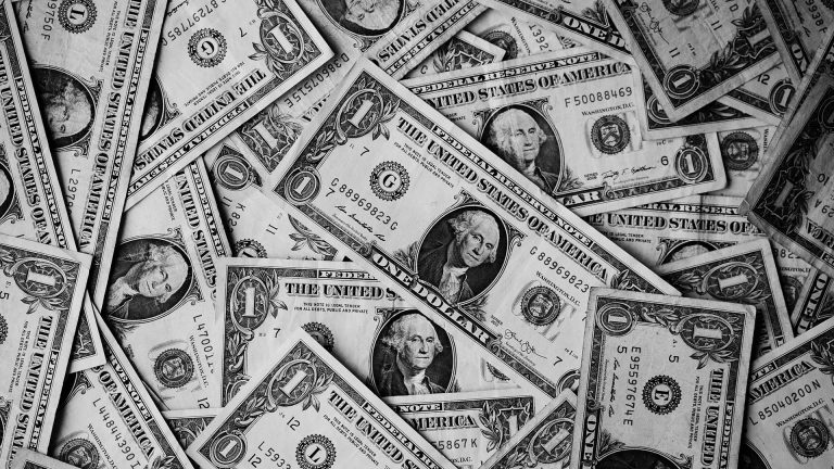 Black and white close-up photo of a scattered pile of United States one-dollar bills.