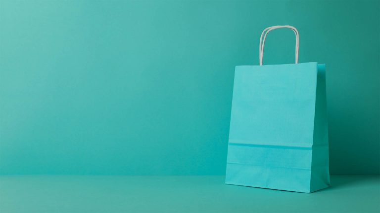 A teal-colored paper shopping bag with white handles, set against a matching teal background.