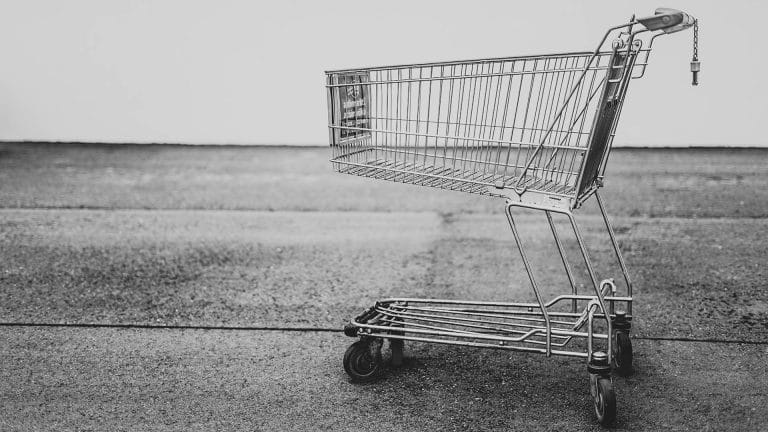 Black and white photo of an empty metal shopping cart on an asphalt surface.