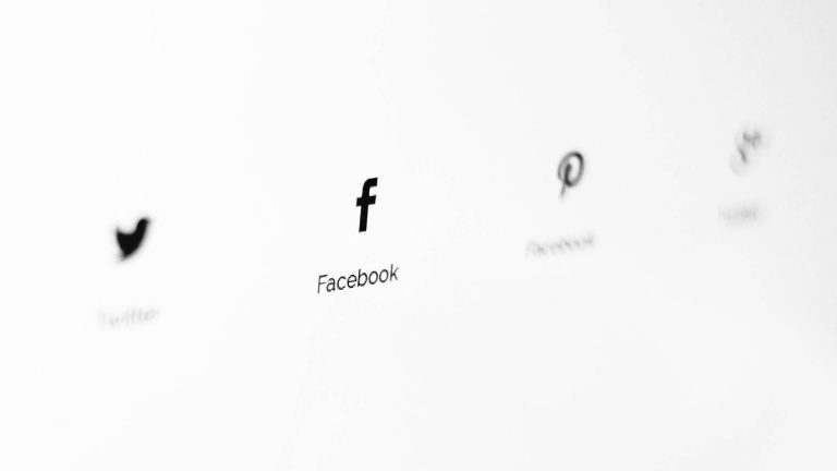 Black and white close-up of social media icons on a screen, with the Facebook logo in sharp focus.