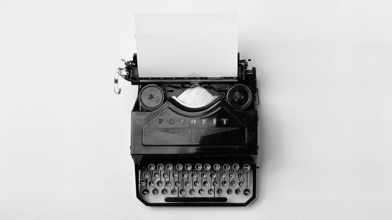 Black and white top-down photo of a vintage typewriter with a blank sheet of paper loaded in it.
